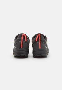 Chaussures de trail avec une tige noire et beige, des accents rouges, un tissu texturé et une semelle en caoutchouc noir robuste pour une meilleure traction.