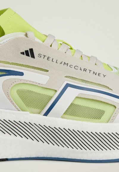 Lightweight sneaker with a beige upper, green mesh accents, blue detailing, and textured white sole with black stripe patterns.