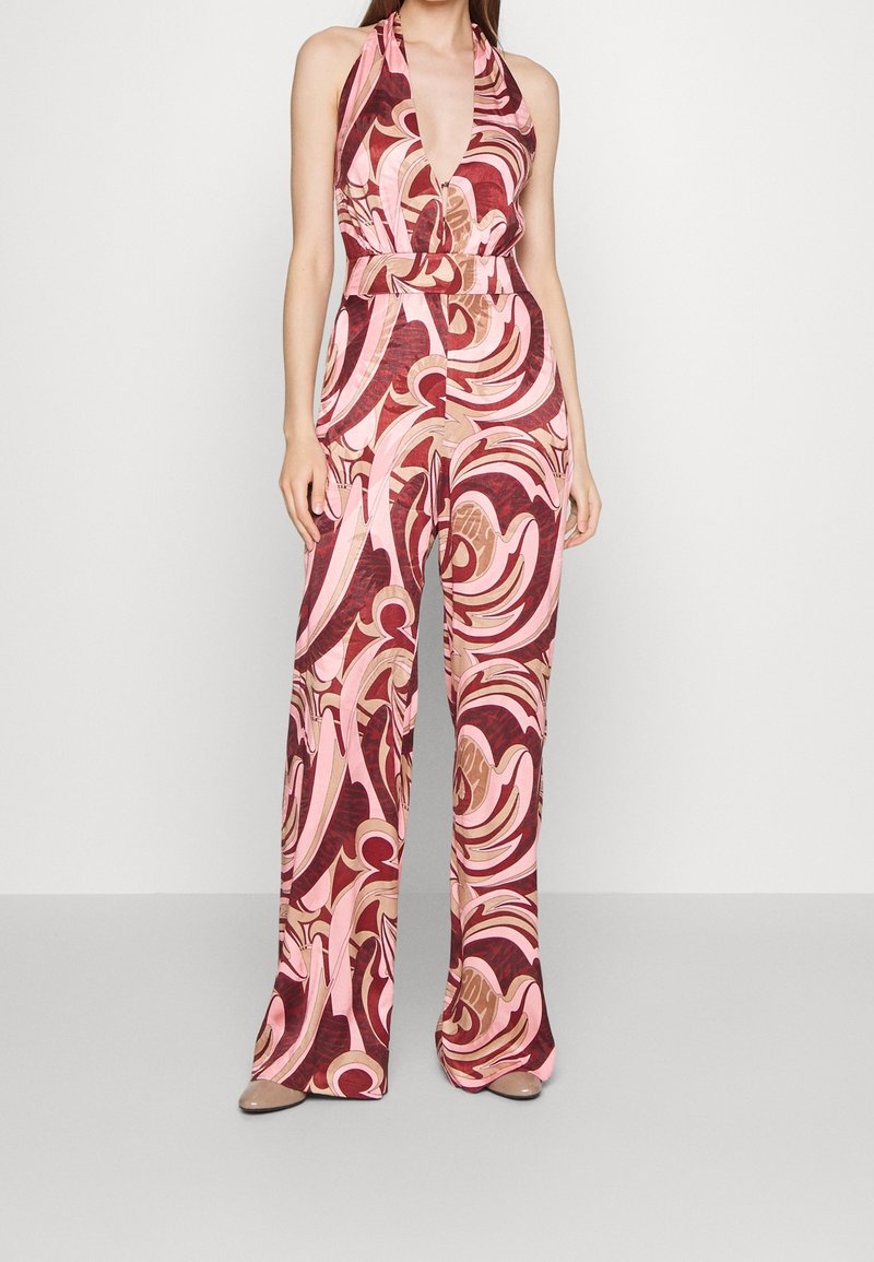 Combinaison à col licou avec un décolleté en V profond, arborant un motif tourbillonnant rose, rouge et marron ; jambes évasées et taille cintrée.
