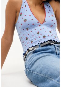 Ljusblå kort topp med jordgubbstryck, ribbad textur och vågig nederkant. Matchad med högmidjade denimjeans och ett svart bälte.