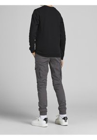 Sort crewneck sweatshirt med lange ærmer, grå cargo-bukser med sidelommer og hvide sneakers med sorte accenter.