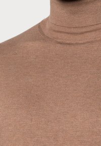 Brun polotröja med ribbad struktur. Närbild visar den åtsittande kragen och sömlösa designen utan synliga detaljer.