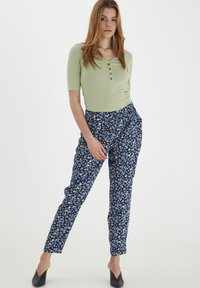 Top corto a righe verde con maniche corte e bottoni, abbinato a pantaloni blu con motivo floreale. Vestibilità slim e vita elastica. Ballerine nere a punta.