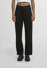 Černé široké kalhoty s plisováním, zapínáním na knoflík a hladkým povrchem. Nosené s krátkým bílým topem a černými platformovými botami.