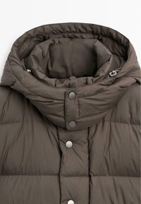 Hnědá péřová bunda s vysokým límcem, druky a prošívanou texturou. Materiál působí měkce a izolovaně, vhodný do chladného počasí.