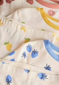 Drie T-shirts met korte mouwen gestapeld, met fruitpatronen. Kleuren omvatten roze, geel en blauw op een crème achtergrond, met contrasterende halslijnen.