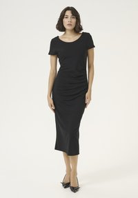 Robe midi noire, ajustée avec des manches courtes et un col rond, mettant en avant un ruché sur les côtés pour ajouter de la texture et un fini en tissu lisse.