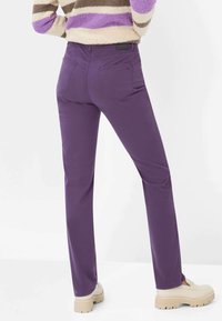 Pantaloni di cotone viola a vestibilità slim, con due tasche posteriori e una texture liscia. Abbinati a scarpe platform color bianco sporco.