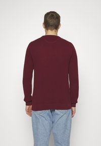 Bordeaux breigoed trui met een structuuroptiek, ronde hals en lange mouwen; gedragen over lichtblauwe denim jeans.