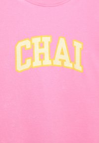 Roze katoenen T-shirt met het woord "CHAI" in vetgedrukte, boogvormige gele letters. Gladde textuur met een ronde hals.
