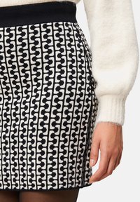 Wollrock in Schwarz und Weiß mit geometrischem Muster. Verfügt über einen einfarbigen schwarzen Bund und strukturierte Stoffoberfläche, seitlich betrachtet.