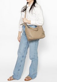 Beige leren handtas met een gestructureerde vorm, voorzien van zilveren hardware details en een afneembare schouderband, gecombineerd met casual jeans.