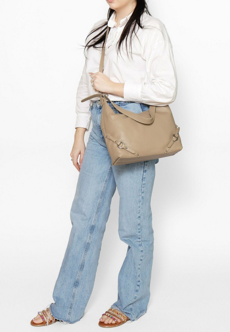 Beige leren handtas met een gestructureerde vorm, voorzien van zilveren hardware details en een afneembare schouderband, gecombineerd met casual jeans.