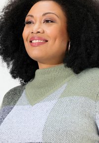 Hellgrüner Strickpullover mit V-Ausschnitt, der ein geometrisches Muster in Grautönen und Weiß zeigt, aus strukturiertem Stoff und mit geripptem Kragen.