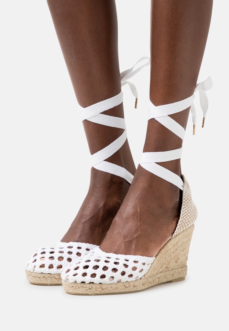 Espadrillas bianche a zeppa con una texture intrecciata e un motivo a reticolo aperto. Presentano lacci in raso bianco legati attorno alle caviglie. Suola in iuta naturale.