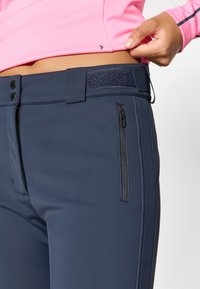 Tmavě modré uplé kalhoty s hladkým povrchem, s kapsou na zip, zapínáním na knoflík a akcentem v podobě suchého zipu na pase.