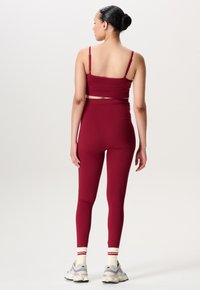 Dieprode crop top met spaghettibandjes en hooggeknipte legging, beide in een gladde, rekbare stof; model draagt grijze sneakers met witte sokken.