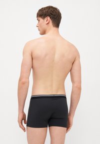 Schwarze Herren-Trunk-Unterwäsche mit einem elastischen Bund in Weißstreifen, die ein glattes, passgenaues Design und mittellange Beine bietet.