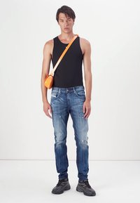 Čierne tielko, vyblednuté modré džínsy s opotrebovanými detailmi, oranžová crossbody taška a šedé tenisky. Jednoduchý, neformálny outfit s živými akcentmi.