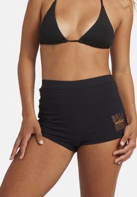 Pantaloni da bagno neri a vita alta con tessuto testurizzato e logo ricamato in arancione e giallo sul lato.