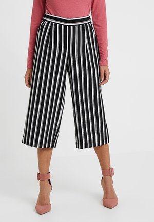 Culottes rayés noir et blanc avec une taille haute et une coupe évasée ; assortis à des chaussures à bride de cheville roses.