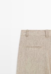 Beige linnenbroekgedeelte met tailleband, lussen voor een riem en een enkele horizontale paspelzak aan de achterkant, op een witte achtergrond.