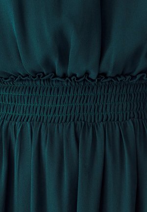 Vihreä kangas, jonka pinta on sileä, ja jossa on kerroksellinen smokkivyötärö ja aallottuvat laskokset alapuolella. Yksinkertainen muotoilu, ilman kuvioita.