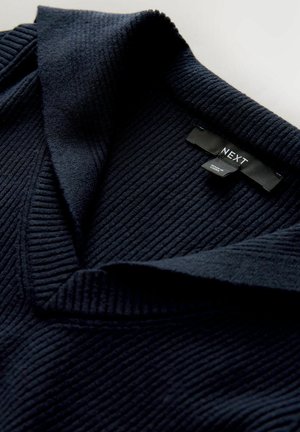 Mörkblå ribbad tröja med bred krage och en etikett som visar "NEXT." Mjuk textur med en strukturerad design och vertikal ribbning.