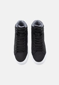 Černé vysoké tenisky se hladkým vnějším materiálem, bílou podrážkou, šedou fleecovou podšívkou a černými tkaničkami. Minimalistický design bez log. 