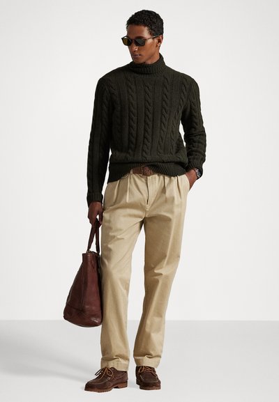 Temno zelena turtleneck pulover iz pletenine, bež nabran hlače, rjava usnjena torba, rjava čevlji z oranžnimi vezalkami, sončna očala.