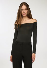 Body nero smanicato con maniche lunghe, realizzato in un materiale liscio e elasticizzato, abbinato a pantaloni neri su misura.