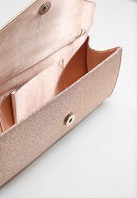Rose guld clutch-väska med metallisk finish, tryckknappsstängning och fodrad med satin inuti. Har en sidofack och slät yta.