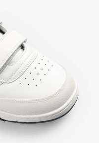 Weißer Sneaker mit einem Obermaterial aus glattem Leder, strukturierten Akzenten, Klettverschlüssen, perforiertem Zehenbereich und einer Gummisohle.