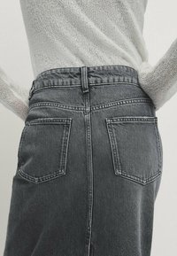 Jupe en denim grise taille haute avec deux poches arrière, détails cousus et une silhouette ajustée. Texture lisse et légère élasticité visible.