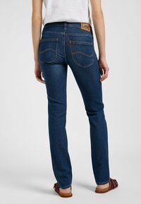 Jeans de mezclilla azul oscuro con un diseño de pierna recta, que cuentan con una etiqueta de cuero marrón en la cinturilla y dos bolsillos traseros con costuras amarillas.