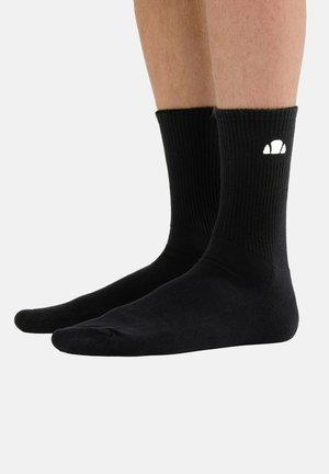 Schwarze Socken bis zur Mitte der Wade, an den Füßen getragen, mit einem kleinen weißen Logo an der Außenseite jeder Socke vor einem einfarbigen Hintergrund.