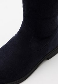 Bottine en daim bleu marine avec une texture lisse, un bout arrondi et des détails de couture subtils. Semelle en caoutchouc noire pour une meilleure adhérence.