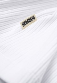 Tissu blanc côtelé avec une petite étiquette beige affichant le texte "HK84DK10" en lettres noires.