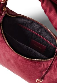 Red leather handbag with a textured surface, featuring a gold zipper and a black patterned interior with a small branding tag.