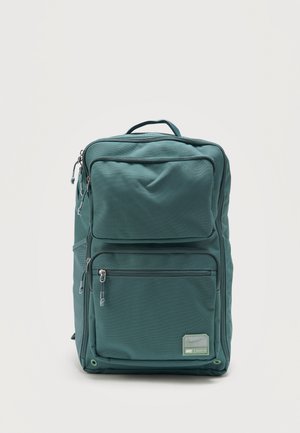 Sac à dos rectangulaire vert avec deux poches avant zippées et une poignée supérieure, présentant un petit patch logo Nike Utility 2.0 sur la poche inférieure.