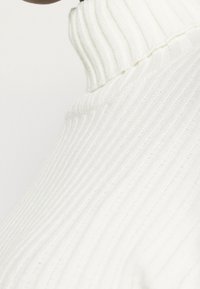 Gestreifter weißer Rollkragenpullover mit hohem Kragen und glatter Textur, der dezente Nahtdetails entlang der Nähte aufweist.