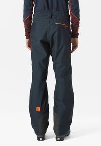 Voděodolné lyžařské kalhoty v tmavě modré barvě s oranžovými akcenty. Mezi rysy patří kapsa na zip a zesílené černé dolní části nohavic.