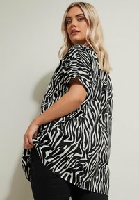 Maglietta a righe zebrate in bianco e nero con maniche corte, vestibilità ampia, orlo curvo e texture morbida, abbinata a pantaloni neri.