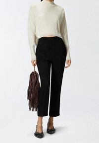 Krämfärgad kortärmad tröja, svarta skräddarsydda byxor, svarta dekorerade lägenheter och en brun fransad handväska med guldchain.