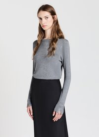 Top grigio a maniche lunghe realizzato in tessuto morbido, con scollatura a girocollo e polsini aperti, abbinato a una gonna nera fluida.