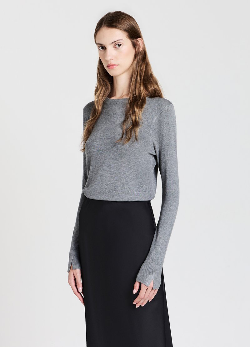 Top grigio a maniche lunghe realizzato in tessuto morbido, con scollatura a girocollo e polsini aperti, abbinato a una gonna nera fluida.