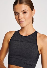 Mörkgrå sportig crop top med mesh-detaljer, sömlös textur och logotyp längst ner. Racerback-design och stödjande passform för aktiv träning.