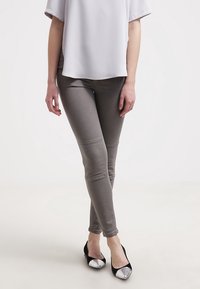 Grå tajta byxor med ribbad detaljering vid låren, kombinerat med en kortärmad vit topp och svarta lägenheter med metalliska spetsar.