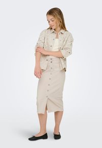 Šviesiai smėlinis mygtukų užsegamas švarkas su raštuotomis išpjovomis, derinamas su atitinkamu smėlio spalvos midi sijonu, kuriame yra mygtukų detalės ir sklendimas. Juodi butai.