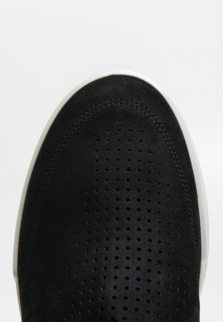 Svart nubuck sneaker med perforerat överdel, vit gummisula, rund tå och sydda detaljer längs kanten.